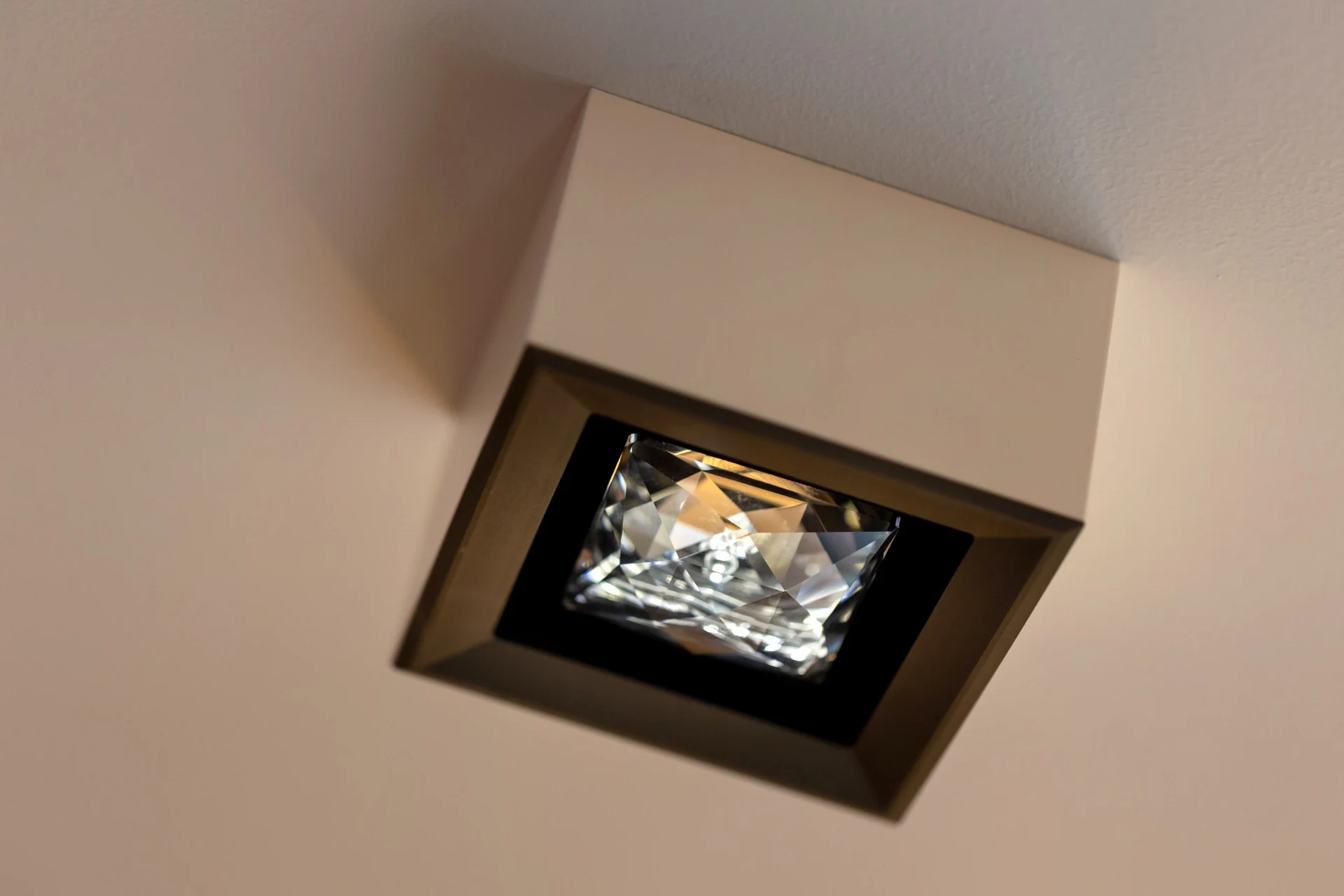MOIRA IRIS surface-mounted ceiling spotlight with a white housing, bronze front and square faceted crystal, viewed from below.